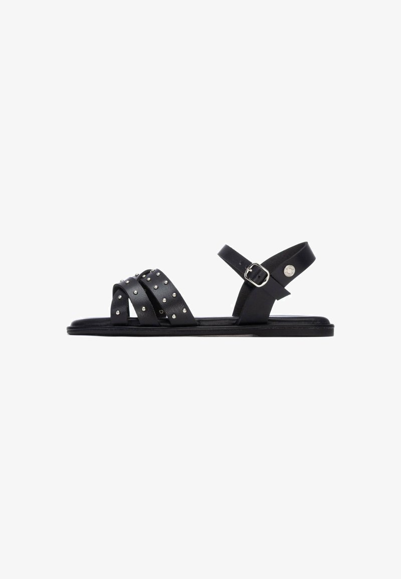 Sandalias de cuero negro con tres tiras anchas con tachuelas plateadas, una correa en el tobillo con hebilla y una suela plana. Diseño sencillo y moderno.