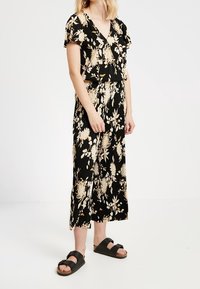 Černé květinové šaty s krátkými rukávy, s výstřihem do V a volným střihem. Zlaté a krémové květinové vzory zvýrazňují látku.