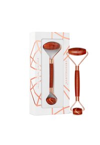 Gemstone facial roller with a deep orange stone, gold-tone metal handle, and a sleek design; packaged in a box with geometric accents.