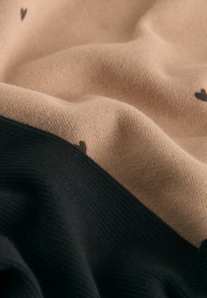 Gros plan sur un tissu tricoté doux avec des sections beige et noir, présentant de petits motifs en forme de cœur noirs sur la zone beige.
