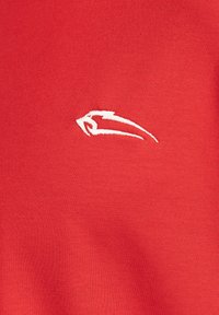Camiseta de tela texturada roja con un pequeño logo bordado en blanco en el lado izquierdo. Diseño de cuello redondo simple, adecuado para uso casual.