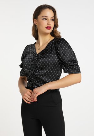 Musta, satiini bluus, jossa on V-muotoinen kaula-aukko, rypistetty etuosa ja puffattuja lyhyitä hihoja, joissa on geometrinen hopeinen kuvio. Yhdistetty mustiin housuihin.
