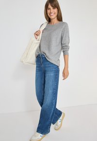 Maglietta grigia a maniche lunghe con righe, jeans blu a gamba larga e borsa a tracolla di colore crema con texture. Le calzature presentano accenti crema e blu.