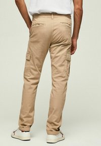 Beige cargobyxor med rak bendesign, utrustade med cargo-fickor på sidorna och baksidan, tillverkade av bomullstyg, kombinerade med vita sneakers.