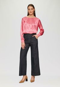 Rosa Satinbluse mit leichten Falten und langen Ärmeln, kombiniert mit weiten, dunkelblauen Denim-Hosen. Das Model trägt braune Blockabsatzschuhe.