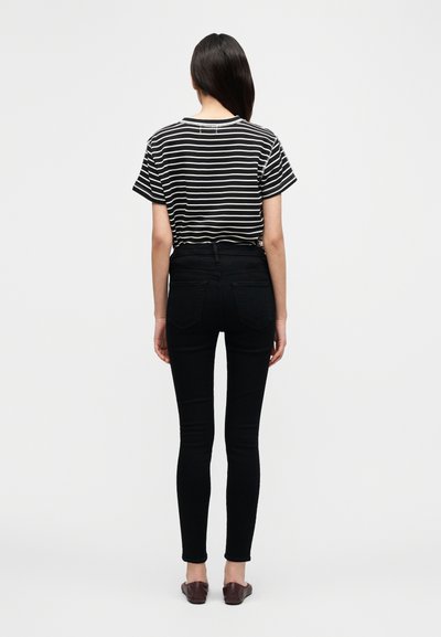 Μαύρο-άσπρο ριγέ μπλουζάκι με κοντά μανίκια, σε συνδυασμό με μαύρο τζιν ψηλόμεσο και καφέ επίπεδα παπούτσια, από πίσω.