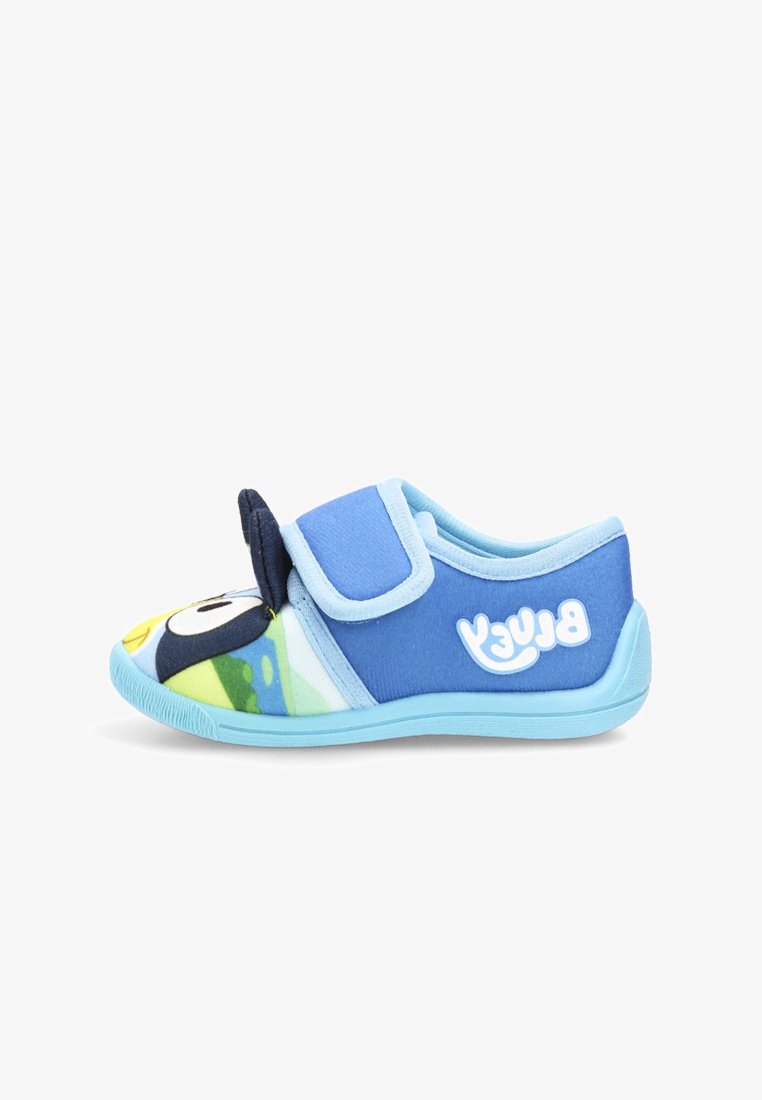 Zapatilla infantil azul con cinta de velcro, cara de pingüino de dibujos animados en la punta y texto "Bluey" en el lado, sobre fondo blanco.