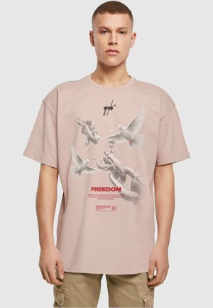 Lyserød oversized t-shirt lavet af bomuld, med et grafisk design af duer og kæder, med teksten "FREEDOM" trykt i rød.