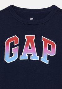 Μπλε βαμβακερό t-shirt με μεγάλο λογότυπο «GAP» σε διαβάθμιση από κόκκινο σε ανοιχτό μπλε. Λαιμόκοψη crew με απαλή υφή και καθαρές λεπτομέρειες ραφών.