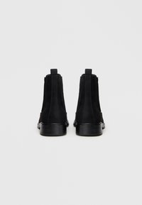 Čierne nubukové členkové topánky s elastickými postrannými panelmi, hladkou čiernou podrážkou a sťahovacími pútkami na chrbte. Obsahujú prešívanie na stranách.