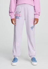 Pantaloni della tuta viola chiaro con cintura elastica, caratterizzati da grafiche colorate: la scritta "THE COOL", disegni di fiori, stelle e corone. Tessuto di cotone.