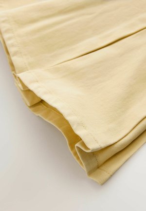 Tissu jaune clair plié avec coutures et ourlet visibles, présenté en gros plan sur un fond clair uni.