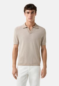 Beige kortærmet polo skjorte med v-halsdesign og tekstureret strikstof. Diskret krave med en glat finish. Ingen synlige detaljer.