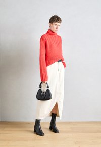 Roter Strick-Turtleneck-Pullover, cremefarbener Midirock mit Schlitz, schwarze Stiefeletten mit Absatz und eine kleine schwarze Handtasche mit metallischen Akzenten.