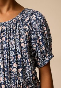 Blommönstrad klänning med mörkblå bakgrund, försedd med rosa och vita blommor. Korta puffärmar, draperad halsringning och mjukt tyg.