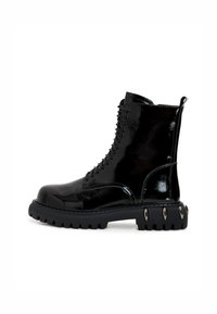 Musta lakattu nilkkabotti paksulla mustalla pohjalla, pyöreällä varvalla ja metallikoristeilla pohjassa. Varustettu nauhakiinnityksellä.