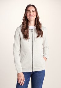 Light grey zip-up hoodie with a soft textured fabric, front pockets, hood, and drawstrings, paired with blue jeans.