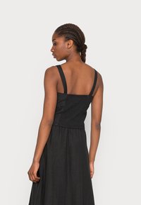 Vestido preto com alças grossas e corpete franzido. A saia flui de forma solta, criando uma textura suave. Design simples e elegante.