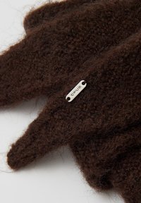 Guanti marroni lavorati a maglia realizzati con un materiale morbido e strutturato. Presentano una piccola targhetta d'argento con la scritta "ORUS" attaccata.