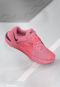 Rosa Sportschuh mit einem Mesh-Obermaterial, strukturiertem Stoff, schwarzen Akzenten und einer gemusterten Sohle. Verfügt über traditionelle Schnürsenkel und einen gepolsterten Kragen.