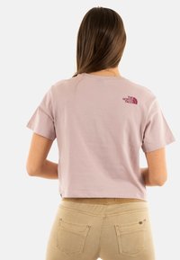 T-shirt cropped a maniche corte in cotone rosa chiaro con un piccolo logo bordeaux sul retro. Abbinato a pantaloni color khaki con tasche posteriori.