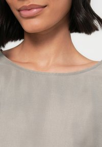 Jasnoszary, gładki materiał o miękkiej fakturze. Posiada szeroki dekolt oraz bezszwowy, zaokrąglony kształt ramion. Minimalistyczne detale.