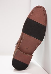 Semelle de chaussure en cuir marron avec une finition texturée. Présente une section en caoutchouc noir et des accents cousus. Taille indiquée comme 42.