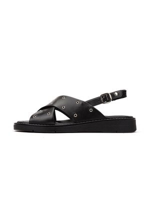 Sandales noires en cuir avec des brides croisées, des clous en argent, une sangle de cheville réglable et une semelle plate noire.