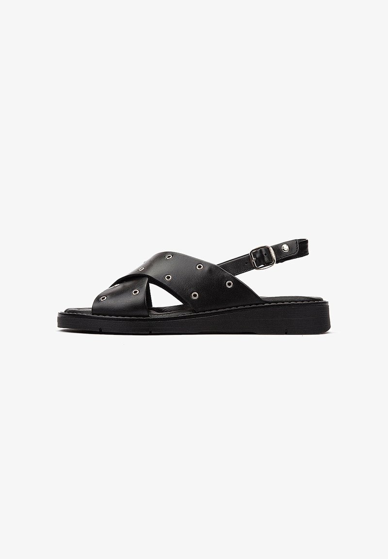 Sandalias de cuero negro con correas cruzadas, tachuelas plateadas, correa en el tobillo ajustable y suela plana negra.
