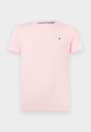 Camiseta rosa claro de manga corta y cuello redondo con pequeño logo de la bandera Tommy Hilfiger en el pecho izquierdo sobre un fondo liso.