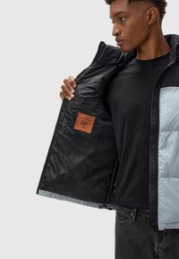 Schwarze und hellblaue Zip-Jacke mit strukturiertem Innenfutter, einem Lederlabel in der Innentasche und einem figurbetonten Design.