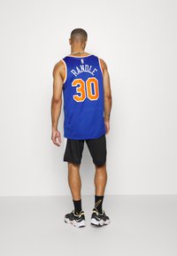 Niebieski strój koszykarski z napisem "RANDLE" i numerem "30" w kolorze pomarańczowym. W zestawie czarne szorty i wielokolorowe buty sportowe. Gładkie tło.