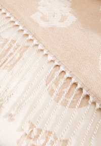 Geweven plaid in zacht beige met een subtiel patroon, voorzien van franjes en een gladde textuur. Lichtgewicht en decoratief.