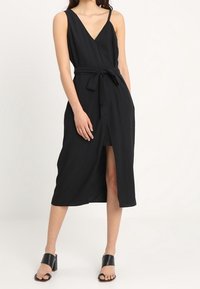 Mustat hihattomat mekot, joissa on V-pääntie, vyötä voitettu vyötäröllä ja etureikä; valmistettu sileästä kankaasta, jossa on rento istuvuus.