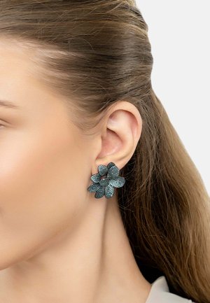 Black floral earrings with textured petals, featuring a layered design and sparkling detailing that catch light, worn on a model's ear.