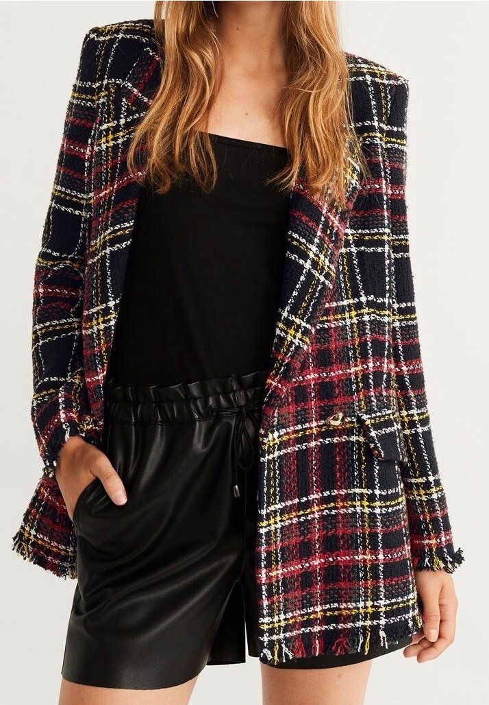 Tweed blazer tummansininen, jossa on punainen ja keltainen ruudullinen kuvio. Siinä on repaleiset reunat, kaarevat läpät ja yksi etutasku. Yhdistetty mustiin shortseihin.