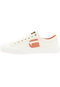 Baskets en toile couleur écru avec une semelle en caoutchouc texturé, arborant un logo orange contrastant et un collier de cheville rembourré.