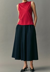 Haut rouge sans manches avec un col rond, associé à une longue jupe fluide bleu marine foncé avec des poches latérales et une texture lisse.