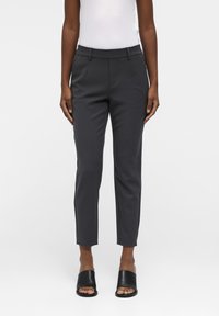 Donkergrijze op maat gemaakte broek met een slanke pasvorm, middelhoge tailleband, zijzakken en een gladde textuur, gecombineerd met zwarte slidesandalen.