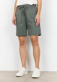 Groene korte broek met elastische tailleband en trekkoord, zijzakken en een relaxed fit. Gecombineerd met witte sneakers op een neutrale achtergrond.