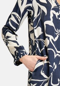 Navyblaues Kleid mit weißem Blumenmuster, langen Ärmeln und lockerer Passform. Es hat einen V-Ausschnitt und seitliche Taschen für Funktionalität.