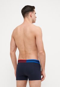 Boxers marine foncé avec des rayures horizontales rouges et bleues sur la bande élastique. Design ajusté, texture douce et sans logos visibles.