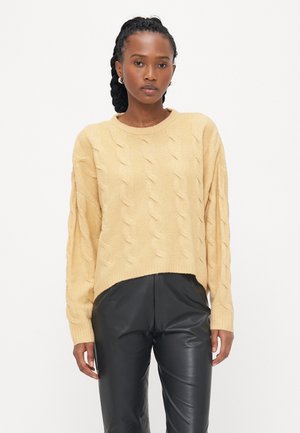Cableknit, lichtgele trui met een ronde halslijn en cropped pasvorm, gecombineerd met zwarte leren broeken. Getextureerde stof met zichtbare stiksels.