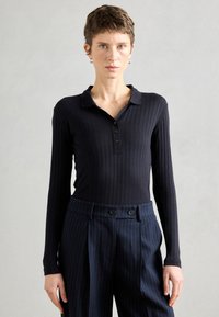 Top de manga longa riscado preto com gola e fecho de botão, combinado com calças azul marinho com riscas e botões duplos.