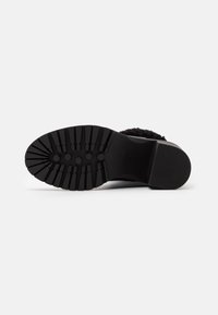 Schwarze Schuhsohle mit gerillter Textur, sechseckigen und länglichen Mustern für Trittfestigkeit sowie einer glatten Ferse für Stabilität.