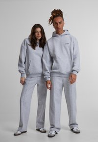 Šviesiai pilki kapučinai ir sportiniai džinsai su raibais rankogaliais, turintys priekines kišenes ir subtilų prekės ženklą. Švelni, pūkuota tekstūra, laisvas siluetas.