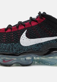 Nike Air VaporMax har en svart och röd stickad ovandel med blå accenter, en vit logotyp och en transparent luftdämpande sula.