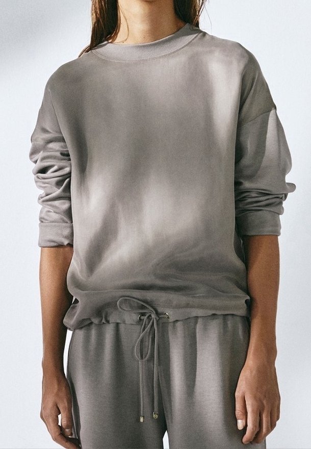 Grijze trui met ronde hals, verzakte schouders, elastische zoom en een trekkoord. Zachte stof met een gladde textuur en een subtiel verloop patroon.