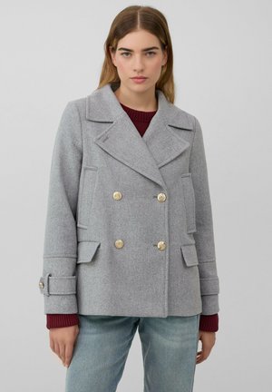 Manteau gris croisé avec de grands revers, boutons dorés et poches avant. Le tissu a une finition texturée. Stylé avec un pull bordeaux.
