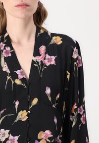 Vestito nero a fiori con fiori rosa e gialli, scollatura a V e chiusura con bottoni. Realizzato in tessuto leggero con una texture morbida.